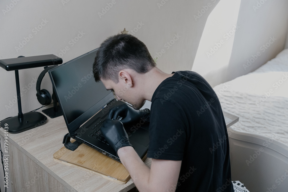 Obraz premium A young man glues stickers to a laptop keyboard with special plastic.