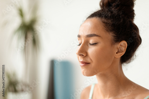 A calm young woman sits quietly with her eyes closed, enjoying a moment of meditation. She appears relaxed and peaceful, embodying a sense of harmony and zen in a tranquil environment.