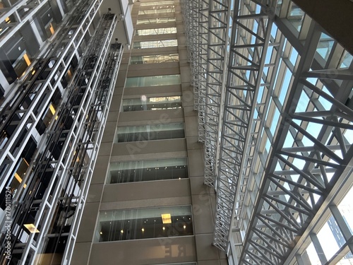 Interior view of a modern building atrium featuring steel beams, glass ceilings, and multiple levels with elevators and offices.