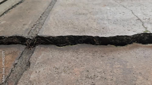 zoomed out view of cement textured concrete ground shows significant damage, with cracks and subsidence on the floor of a home or a street road caused by an earthquake. Close up view