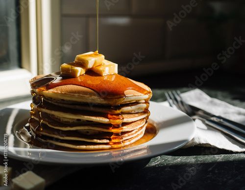 A gourmet breakfast stack of sweet pancakes with maple syrup and butter on a white plate