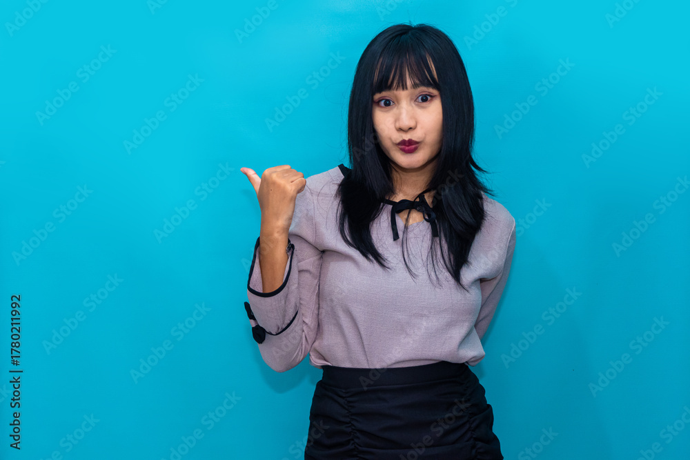 Fototapeta premium A woman gestures with her thumb toward herself while looking surprised. Ideal for self-expression, identity, and influencer-style content.