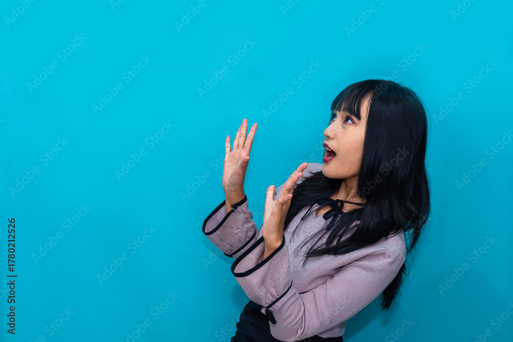 Fototapeta premium The woman reacts in surprise with open eyes and mouth, expressing shock and amazement. Ideal for reaction, lifestyle, and creative advertising.