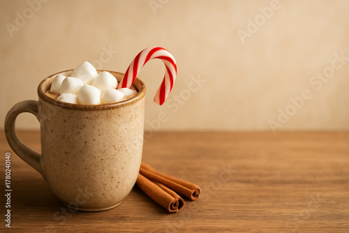 Charming rustic mug filled with hot chocolate, topped with marshmallows and a candy cane. The mug is sitting on a wooden surface with a few scattered cinnamon sticks.