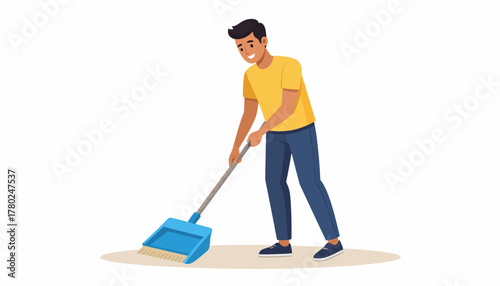 Smiling young man in yellow t-shirt and blue pants sweeping dirt into a blue dustpan with a broom, performing cleaning.