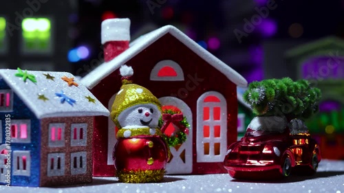 A small Christmas village with decorated colorful houses rotates against the backdrop of a large town