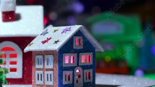 A close-up of a small Christmas village with decorated colorful houses rotating against the backdrop of a large town