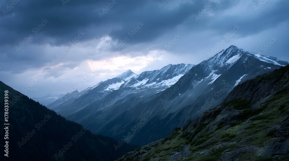 Fototapeta premium Dramatic snow capped mountain peaks under a stormy twilight sky with vast alpine valleys