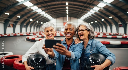 Three mature women taking a selfie at indoor go-kart track. A cheerful photo capturing friendship and fun. Bonding experience, shared laughter, active lifestyle.