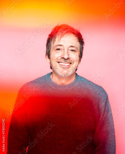 Man in His Mid 50s Smiles Warmly Against a Colorful Background in a Cheerful Setting
