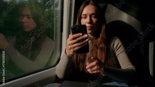Woman travels on train while using smartphone during sunny afternoon journey