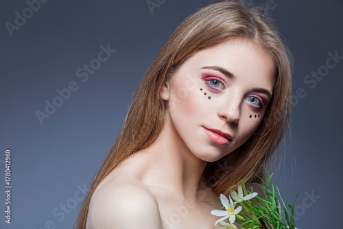 Beauty Concepts. Natural Beauty Portrait of Young and Fresh Caucasian Girl with Vivid Artistic Makeup Against Gray With Flowers
