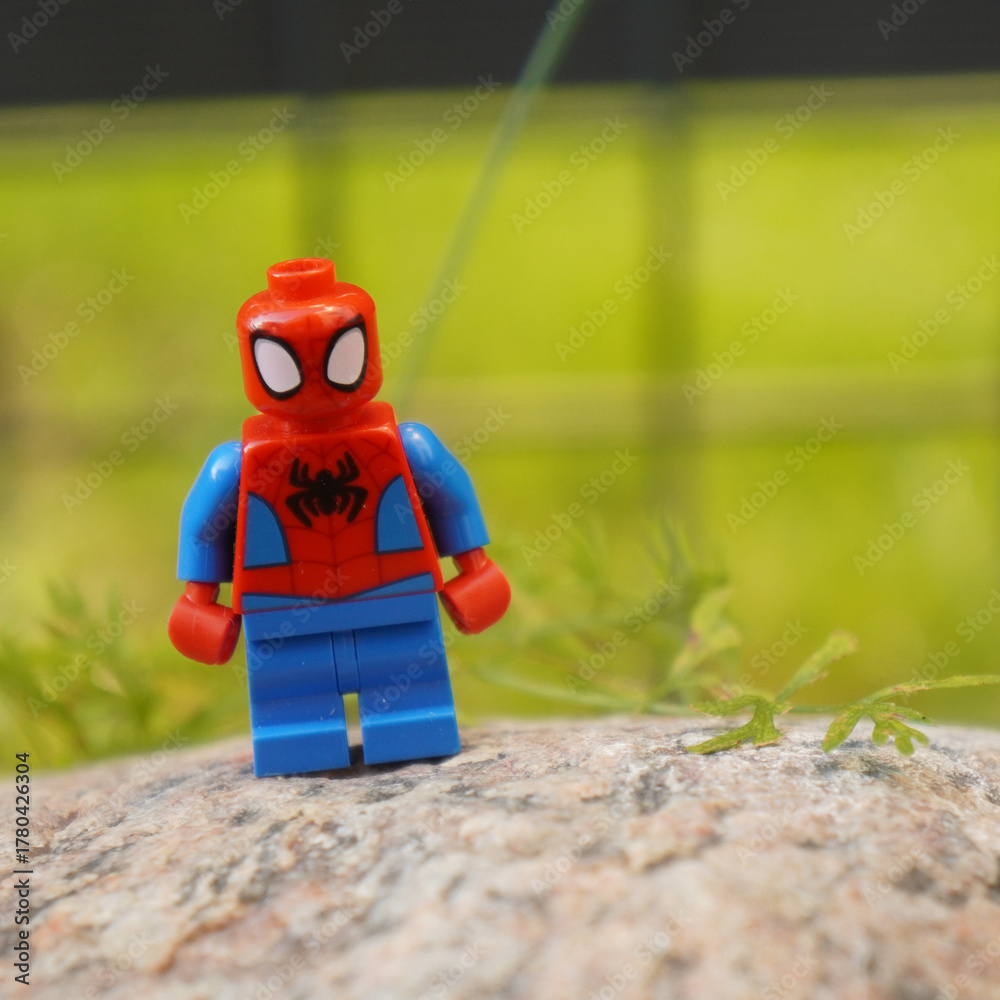 Naklejka premium lego spiderman figure standing on a rock with a blurred green background