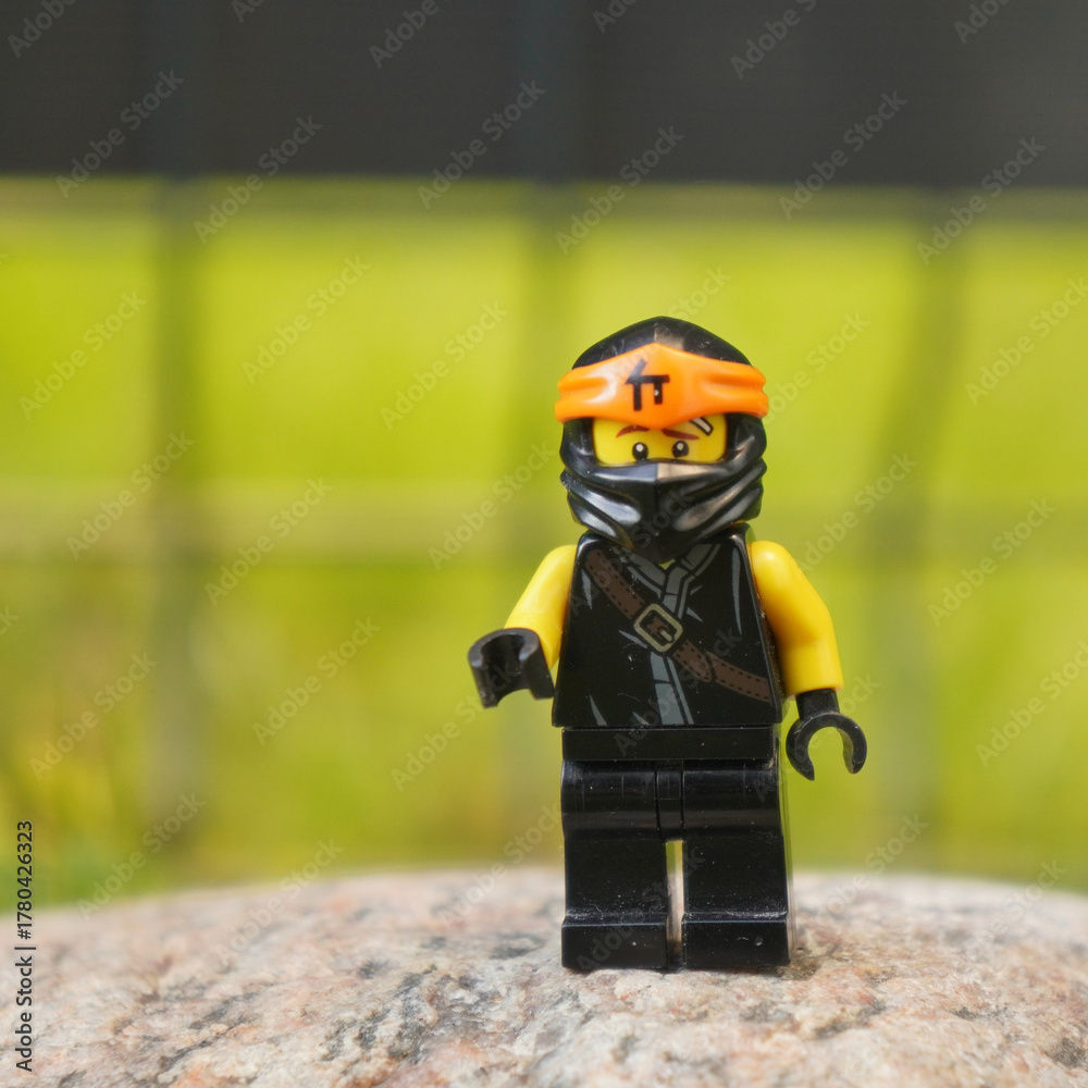 Fototapeta premium Lego Ninjago Jay minifigure standing on a rock with a blurred green background