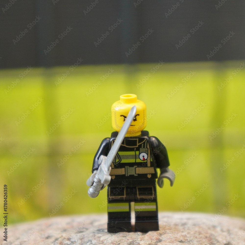 Fototapeta premium Lego firefighter minifigure with a sword, ready for action against a blurry green background