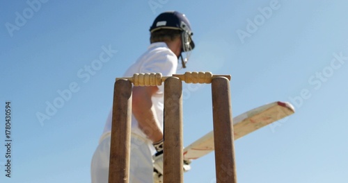 Fotografia Framing cricket wicket with stumps on cricket pitch, batsman wearing white kit,