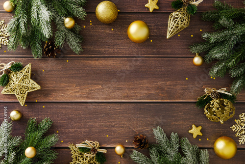 Fotografie Golden baubles, pine branches and stars arranged on wooden surface with empty center