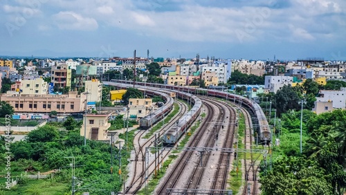 Curved railway tracks lead into the heart of Tirupati city, surrounded by colorful residential blocks and lush greenery. The cloudy sky adds a calm monsoon mood to this vibrant and fast-growing city. 