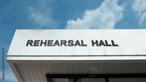 A Rehearsal Hall word sign displayed on a large theater or arts building under a clear blue sky, symbolizing performance practice, drama, music, dance, preparation, and creative arts