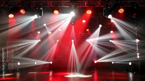 Dynamic stage lighting fills an empty performance venue with vibrant red and white beams cutting through atmospheric haze. Multiple spotlights illuminate the stage floor, creating a dramatic and energ