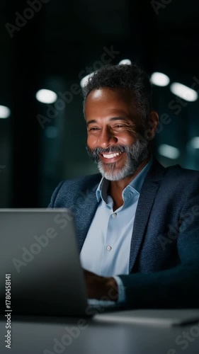 A man is sitting at a desk and using a laptop. He is smiling and he is happy