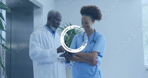 Doctor swiping records on tablet in hospital hall, loading icon showing, nurse pointing for review