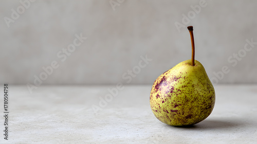 Fresh single ripe speckled pear standing on a light modern minimalist counter, representing concepts of healthy eating, organic food, diet, and simple natural nutrition with copy space