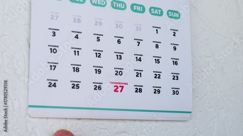 Close-up of male hands tearing off the page of a wall calendar and pointing finger at Thanksgiving 2025 date