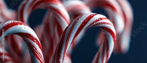 Closeup of festive red and white striped Candy Canes with water droplets on a dark blue background Concept of Christmas, holiday season, and sweet treat