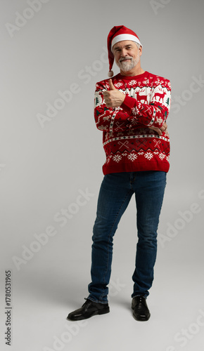 Merry satisfied smiling mature man wear knitted christmas sweater Santa hat showing thumb up. Happy New Year 2026
