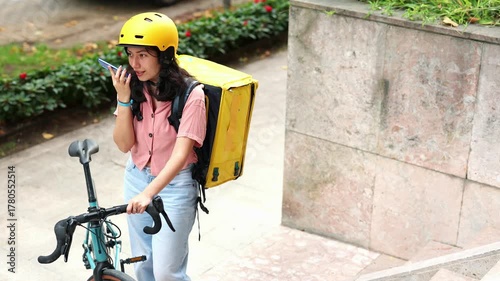 Asian delivery woman with bike speaking on smartphone