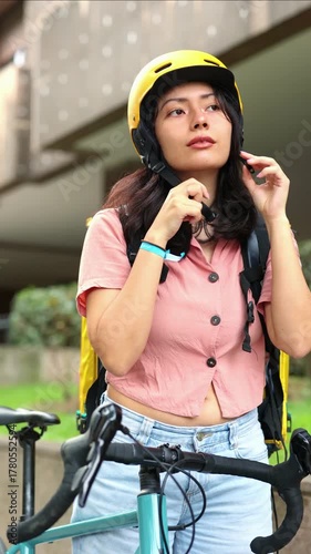 vertical Young delivery woman putting on a helmet for safety before riding her bike