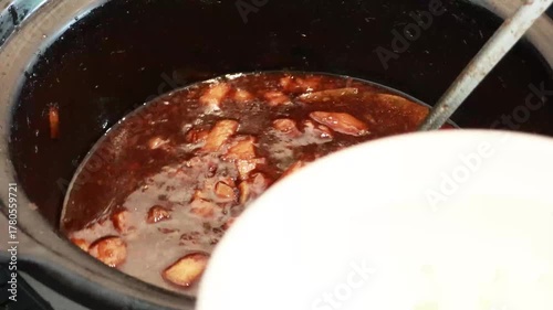 Stirring and pouring braised pork belly meat over cooked rice.