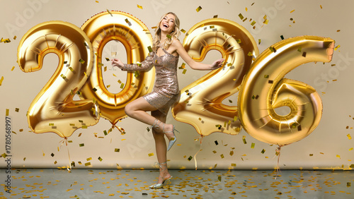 Happy New Year 2026 to you. Beautiful woman in sparkle dress standing under confetti rain with glass of champagne and smiling