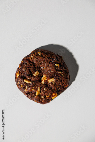 One rich, dark double chocolate cookie with visible nut chunks placed on a white background, casting a soft shadow. No branding or text present