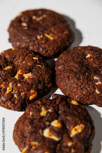 Four rich, dark chocolate cookies with visible nut chunks are arranged closely on a white background, emphasizing texture and ingredients. No branding is visible