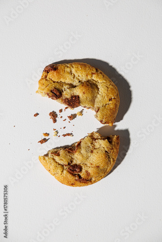 Canvas Print A chocolate chip cookie broken in half lies on a white surface, with scattered crumbs adding a touch of realism