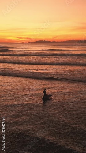 Aerial view of lonely person with surfboard looking at ocean at sunset time, vertical video