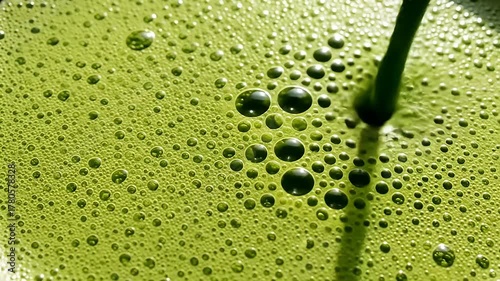 Vibrant green liquid surface filled with many bubbles, stirred with a green stirring stick