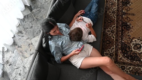 A mother and child share a tender moment on a comfortable sofa, immersed in their own worlds while surrounded by the serene comfort of home.