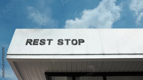 A Rest Stop word sign displayed on a roadside service or travel building under a clear blue sky, symbolizing road travel, breaks, public amenities, transportation, and convenience