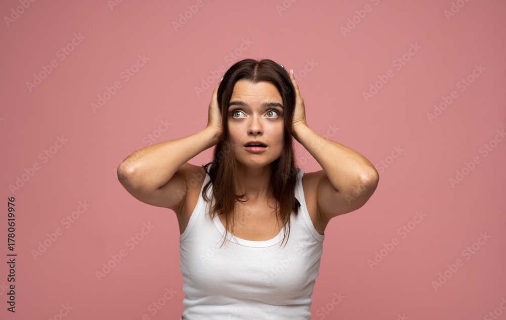 Fototapeta premium Shocked young woman holding head with both hands expressing surprise or panic