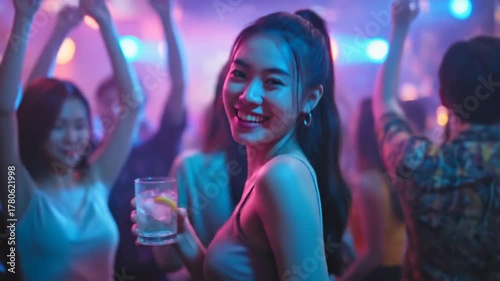 Happy young Asian woman enjoying cocktail drink at lively nightclub under colorful pink neon lights, an exciting evening party and celebration event. Sexy attractive girl dance at asia night club.