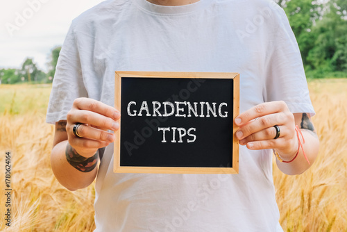 Individual holding a chalkboard sign displaying gardening tips in a golden field of wheat