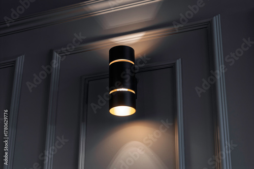 Modern black wall sconce emits soft light on a textured gray wall, creating a cozy, stylish ambiance with gentle upward and downward illumination.