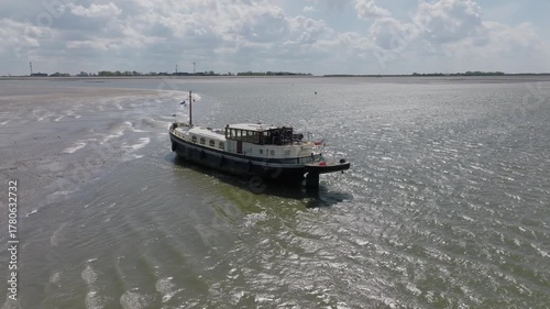 Traditional vessel grounded on shallow tidal flats at low tide; stern three‑quarter perspective in daylight.