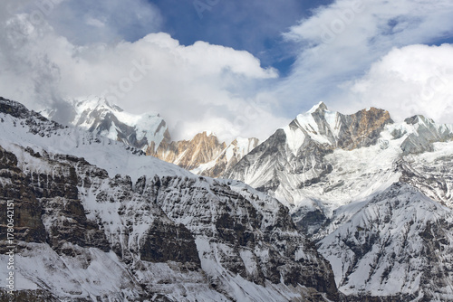 Mountains covered with snow and partial cloud cover under blue sky in Annapurna Sanctuary, Nepal. The area is very mountainous.
