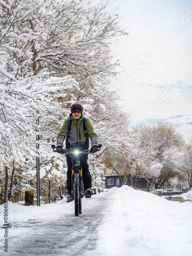 A man rides a bicycle on a winter day along a city alley. After a snowfall. The guy is wearing a bicycle helmet. An active lifestyle in winter.