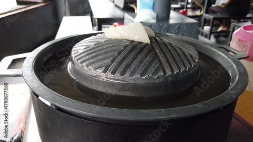 Traditional Thai barbecue grill pan, known as Moo Kratha, with a piece of pork lard melting on top. Popular Thai-style BBQ combining grilling and hotpot cooking in one pan.