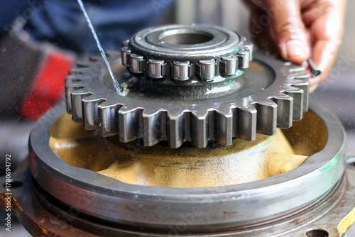 Close-up of a large machine gear and roller bearing being cleaned or lubricated with fluid by a mechanic's hand during the maintenance and assembly process.